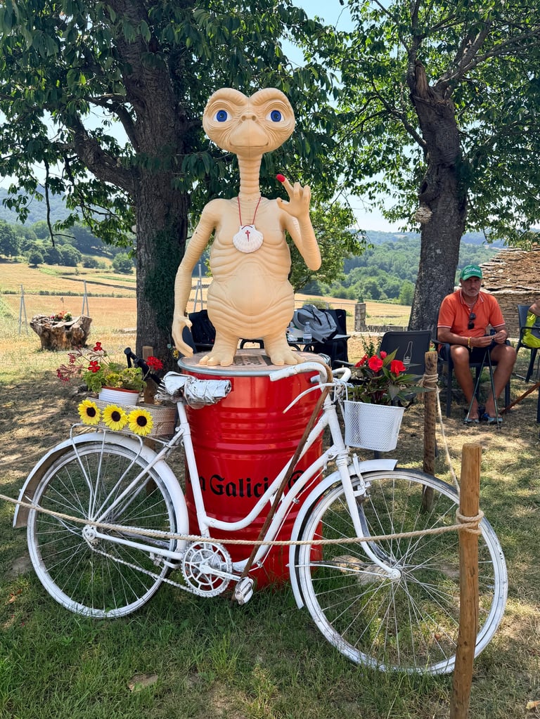 E.T. figurine mounted on a red bicycle with flowers, displayed outdoors in a pastoral landscape setting