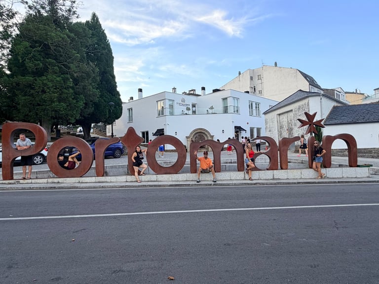 Large red Portorož sign with people posing on a street, historic buildings visible in background