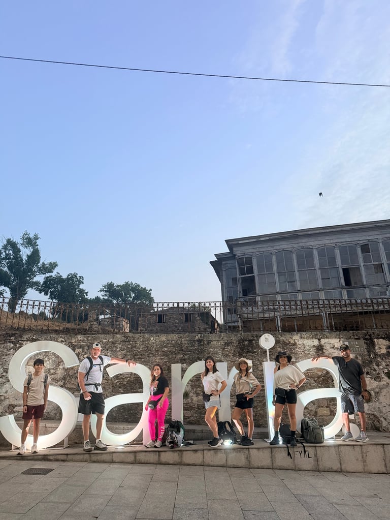 Group of people posing with large white Sarkara letters at outdoor location with historic building in background